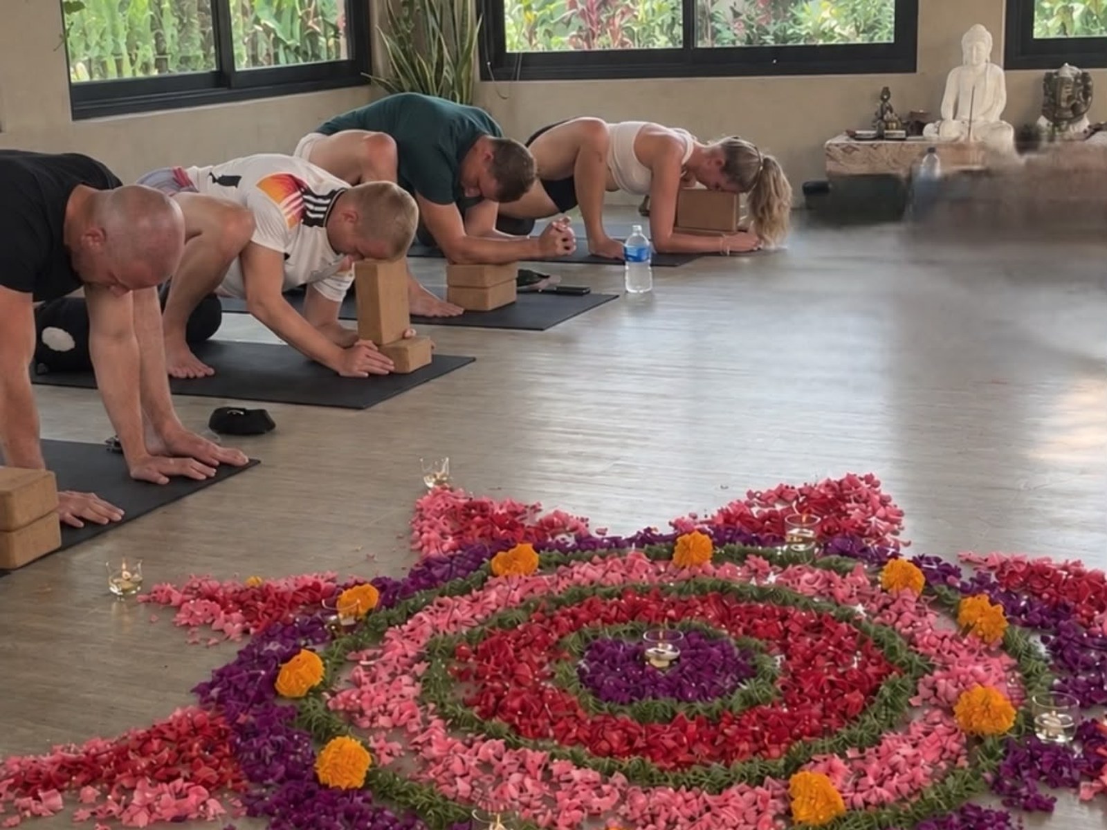 Guests in a yoga class beside a flower mandala in a bright studio in Bali