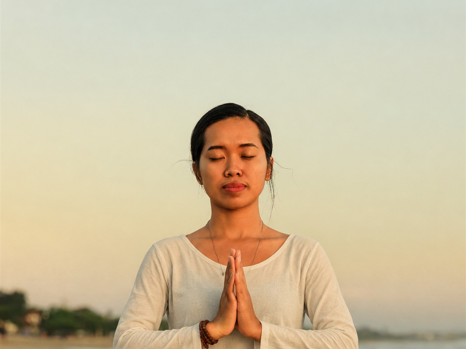 Woman meditating with hands in prayer on a beach at sunset