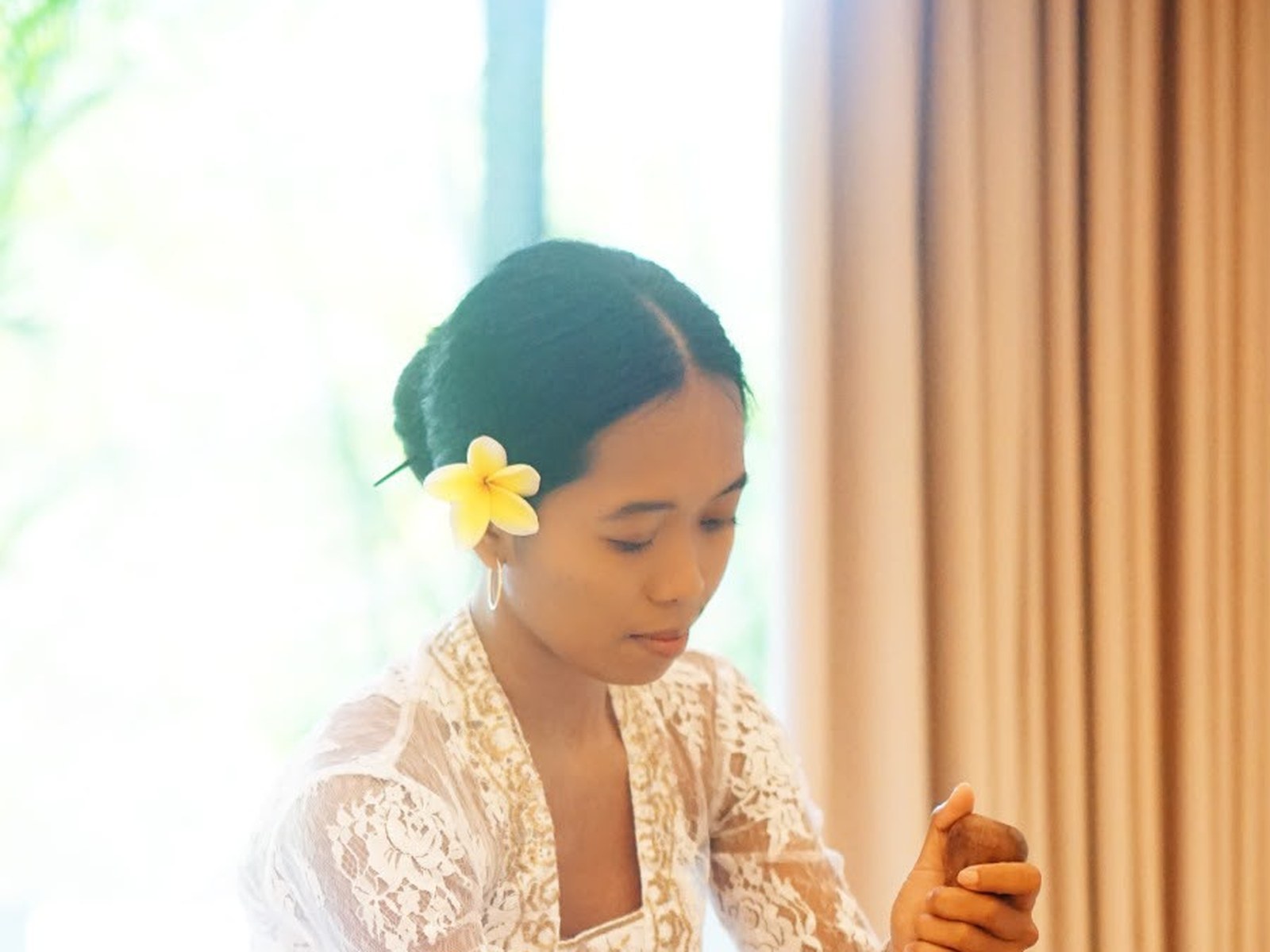 Woman in a lace kebaya playing a Balinese singing bowl surrounded by bronze bowls
