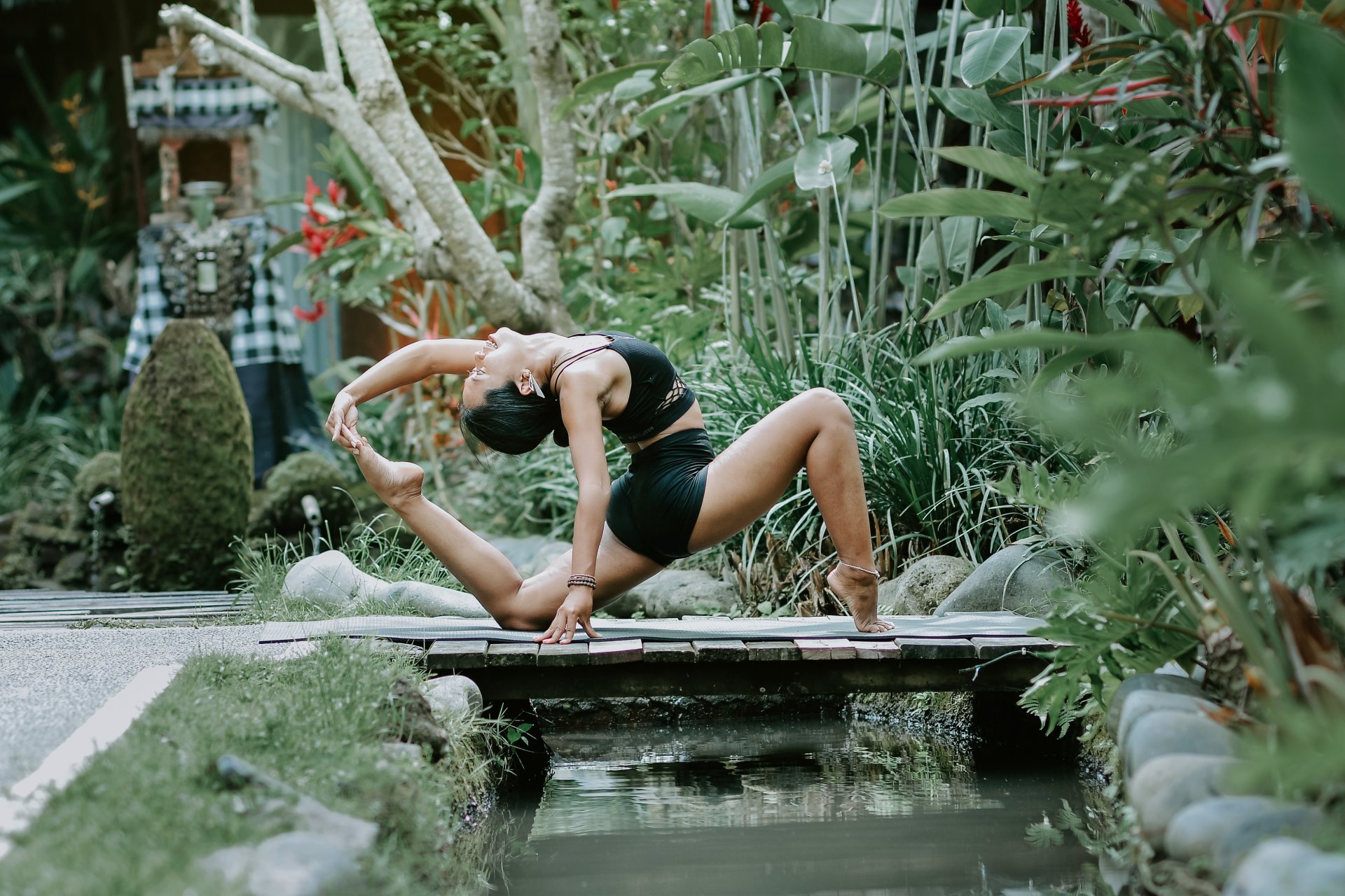Ocha in a yoga pose on a wooden bridge in a Balinese garden